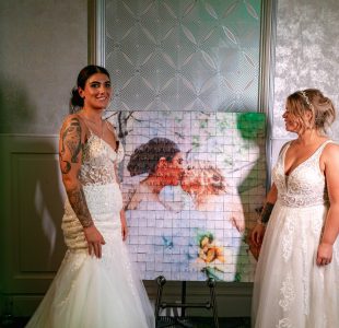 The brides standing beside their finished Mosaic wall photo